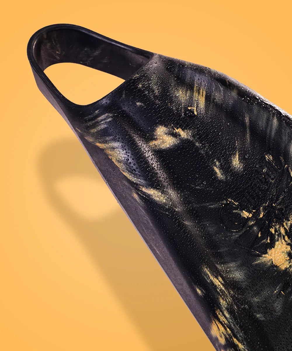 Black and gold swimfin with water droplets on textured surface against yellow background