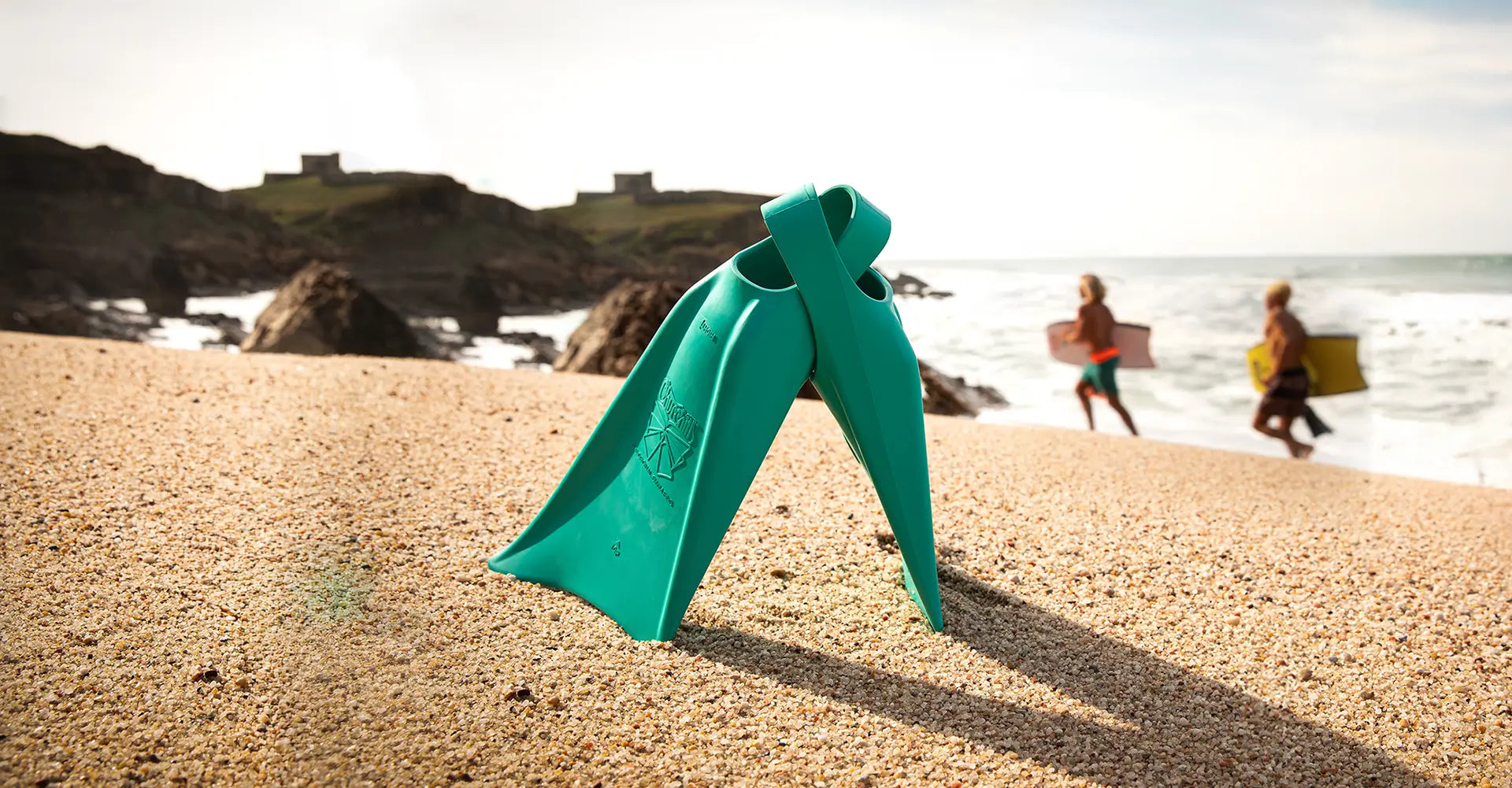 Green diving fin on a sandy beach with people and ocean in the background